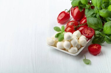 Beyaz ahşap bir masada fesleğenli ve domatesli Mozzarella peyniri. Geleneksel İtalyan atıştırması.