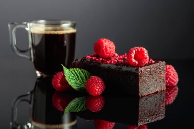Chocolate cake with fresh raspberries and black coffee on a black reflective background.