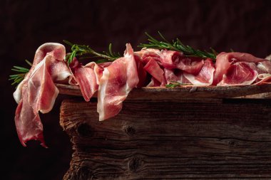 Italian prosciutto crudo or Spanish jamon with rosemary on an old wooden background.