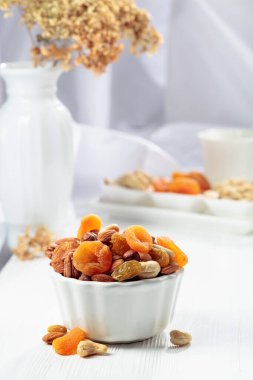 Beyaz ahşap bir masada kurumuş meyve ve çeşitli fındıklar..