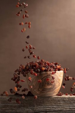 Kahverengi arka planda uçan kuru üzümler. Tahta bir kasede kuru üzümler. Boşluğu kopyala.