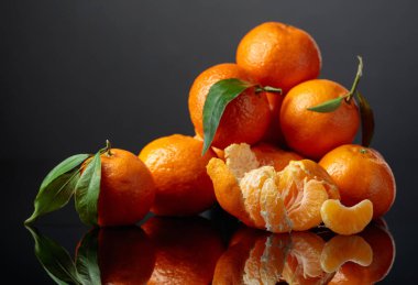 Tangerines or clementines with green leaves on a black reflective background. Copy space.