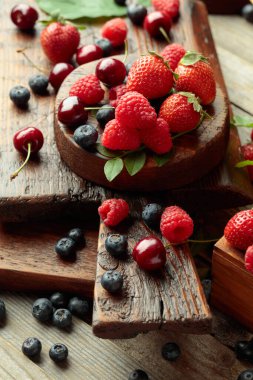Yapraklı taze böğürtlen. Çilek, ahududu, böğürtlen ve kirazlar eski ahşap bir masada.. 