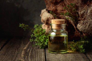 Bottle of thyme essential oil with fresh thyme twigs on an old wooden table. Copy space.