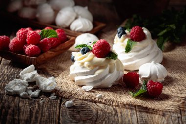 Pavlova 'yı ahududu, yaban mersini ve nane şekeriyle eski ahşap bir masanın üzerine koy.. 