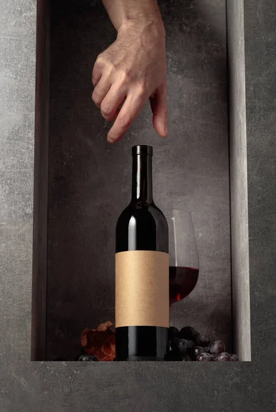 红葡萄酒配蓝葡萄瓶子上有个空标签手伸出手去拿一瓶酒 — 图库照片