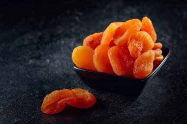 Siyah taş bir masada seramik bir tabakta kurumuş kayısılar..