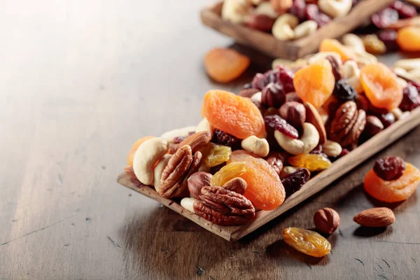 Mix of nuts and dried fruits on an old wooden table. Presented apricots, raisins, walnuts, hazelnuts, cashews, pecans, and almonds.