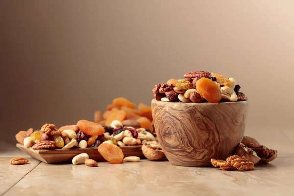 stock image Dried fruits and nuts on a beige ceramic table. The mix of nuts, apricots, and raisins in a wooden bowl. Copy space.