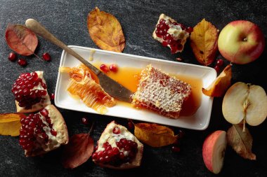 Apple, pomegranate, and honey, are the traditional food for Jewish New Year - Rosh Hashana. Honeycomb and fruits on a black stone table.