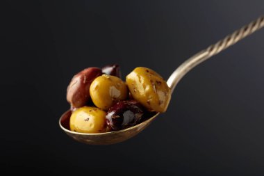 Spicy olives in a big spoon on a black background.