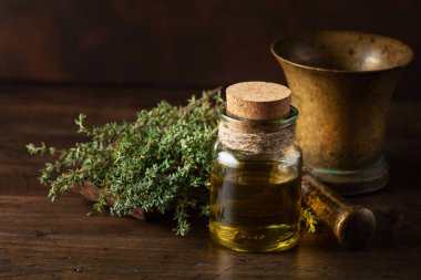 Eski ahşap bir masada taze kekik ile bir şişe kekik yağı..