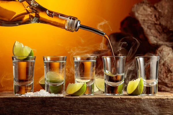 ボトルから金のテキラをグラスに注ぐ 古い板の上に塩とライムのスライスと強いアルコール飲料 — ストック写真