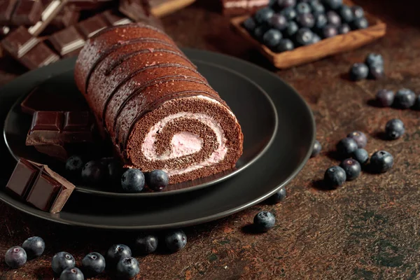 stock image Chocolate roll cake with blueberries and a broken black chocolate bar.