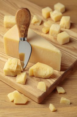 Parmesan cheese and knife on a wooden cutting board.