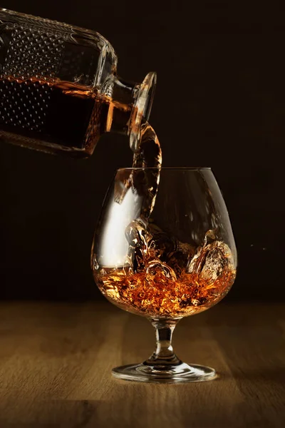Brandy is poured from a decanter into a snifter glass. Cognac on an oak table.