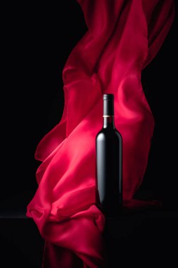 Bir şişe kırmızı şarap ve siyah arka planda kırmızı kumaş..