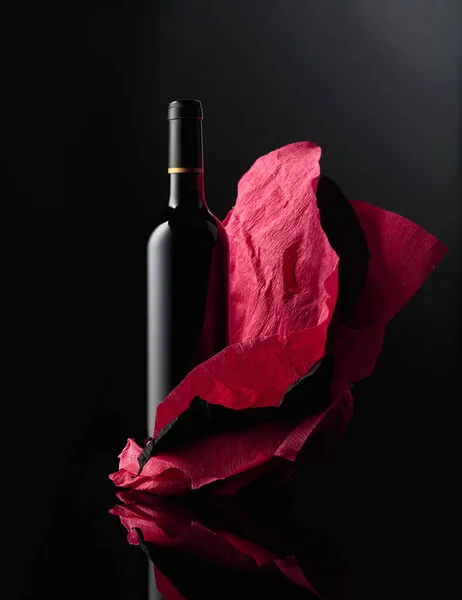 在皱皱巴巴的纸上的一壶红葡萄酒 黑色反光背景 — 图库照片