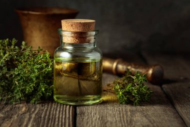 Bottle of thyme essential oil with fresh thyme twigs on an old wooden table.