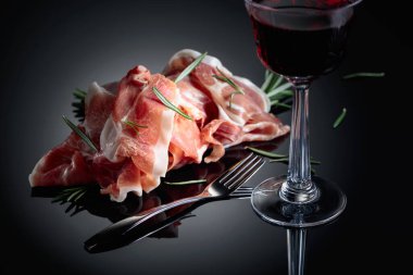 Italian prosciutto or Spanish jamon with rosemary and red wine on a black background.