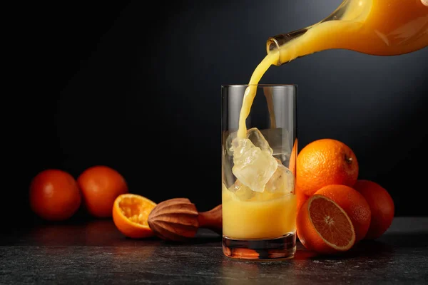 ボトルからオレンジジュースを氷の入ったガラスに入れます コピースペース付き黒の背景 — ストック写真