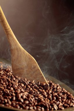 Orta pişmiş kahve çekirdekleri kızartma tavasında dumanlıdır. Boşluğu kopyala.