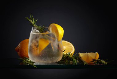 Buzlu, limonlu ve biberiyeli buzlu cin tonik. Siyah arka planda sisli bardakta buzlu, ferahlatıcı bir içecek..