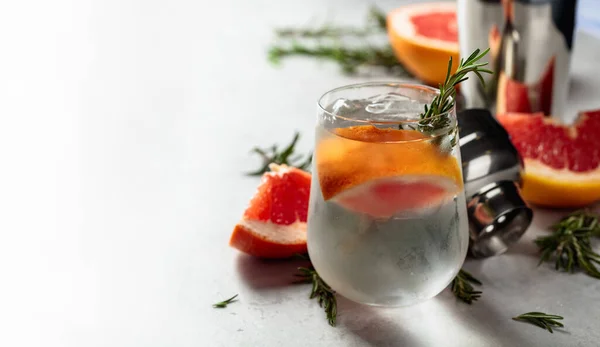 冷たいガラスの中で 天然の氷 グレープフルーツ ローズマリーで飲み物をリフレッシュします 白い大理石のテーブルの上にジンと強壮カクテル — ストック写真
