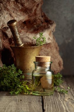 Bottle of thyme essential oil with fresh thyme twigs on an old wooden table.