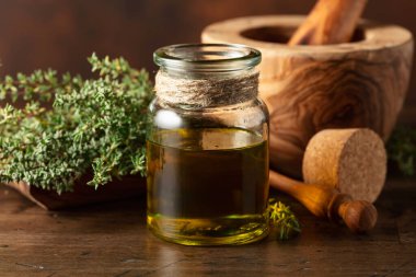 Eski ahşap bir masada taze kekik ile bir şişe kekik yağı..