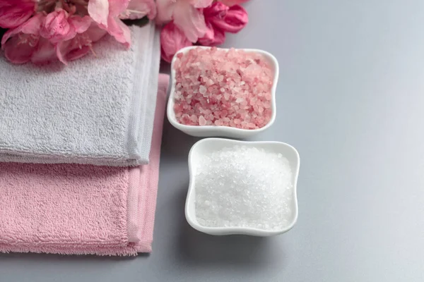 Pembe ve beyaz deniz tuzu, çiçek ve havluyla spa kompozisyonu.