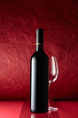 Bottle of red wine and an empty wine glass on a red background.
