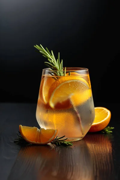 用冰块 迷迭香和橙子装饰在结冰的玻璃杯里 黑色木制桌子上的鸡尾酒玻璃杯 — 图库照片