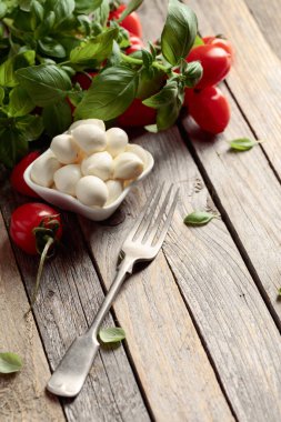 Eski ahşap bir masada fesleğenli ve domatesli Mozzarella peyniri. Geleneksel İtalyan atıştırması.