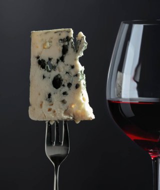 Blue cheese and red wine on a black background.