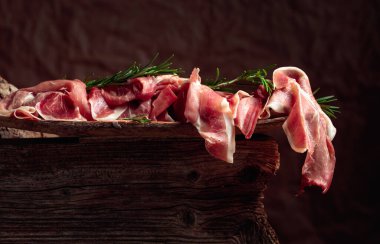 Italian prosciutto crudo or Spanish jamon with rosemary on an old wooden background.