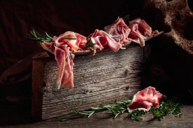 Italian prosciutto crudo or Spanish jamon with rosemary on an old wooden background.