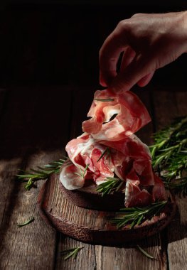 Italian prosciutto or Spanish jamon with rosemary on an old wooden table.