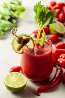 Salatalık, zeytin, limon ve kereviz ile süslenmiş Bloody Mary kokteyli. Beyaz taş bir masanın üzerinde malzemelerle domates suyu..