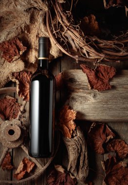 Eski ahşap ve kurumuş asma yapraklarıyla klasik bir arka planda bir şişe kırmızı şarap. Eski şarap kavramı.