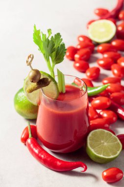 Salatalık, zeytin, limon ve kereviz ile süslenmiş Bloody Mary kokteyli. Beyaz taş bir masanın üzerinde malzemelerle domates suyu..