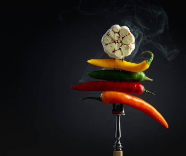 Sarımsaklı kırmızı kırmızı kırmızı biber ve siyah arka planda doğal duman. Baharatlı yemek kavramı.