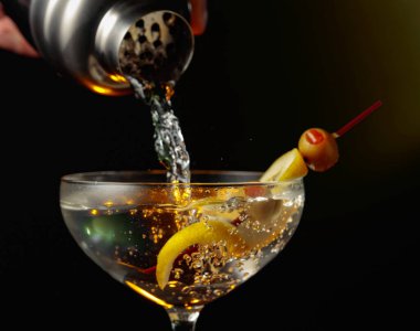 Yeşil zeytinli ve limonlu martini. Kokteyl bardaktan bardağa dökülüyor..