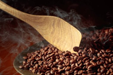 Orta pişmiş kahve çekirdekleri kızartma tavasında dumanlıdır. Boşluğu kopyala.