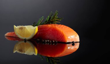 Smocked salmon piece with rosemary, lemon, and peppercorn on a black reflective background.