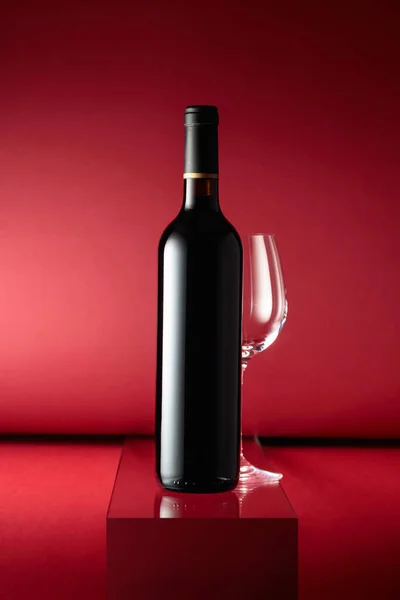 赤い背景に赤ワインと空のワイングラスのボトル — ストック写真