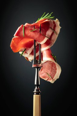 Sliced prosciutto with rosemary on a fork.