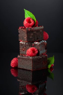 Chocolate cake garnished with fresh raspberries on a black reflective background.