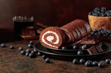 Chocolate roll cake with blueberries and a broken black chocolate bar. clipart