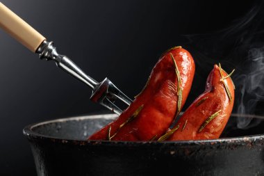 Eski siyah bir tavada biberiyeli kızarmış Bavyera sosisi. Boşluğu kopyala.